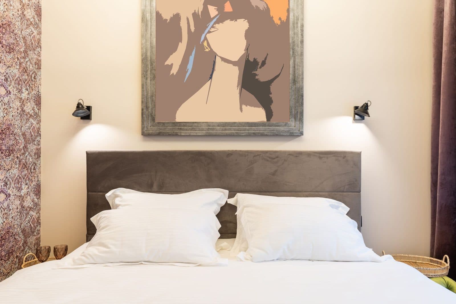 Warm bedroom with a large framed portrait painting centered above the headboard, flanked by two black wall sconces.