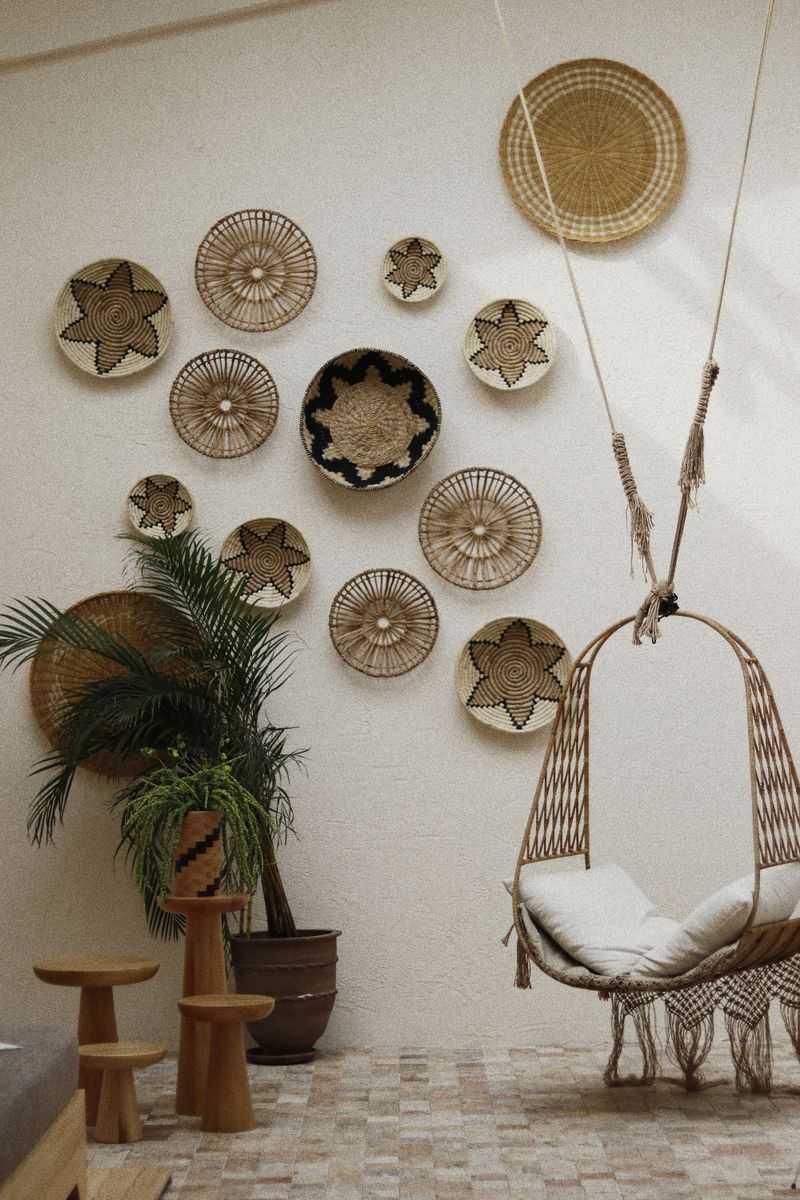Woven straw plates and baskets arranged as wall decor in a bohemian room with a hanging chair and plants