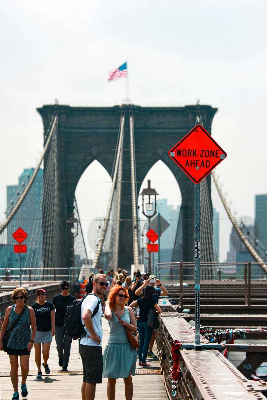 People walking across the Brooklyn Bridge toward its stone towers with the New York skyline behind