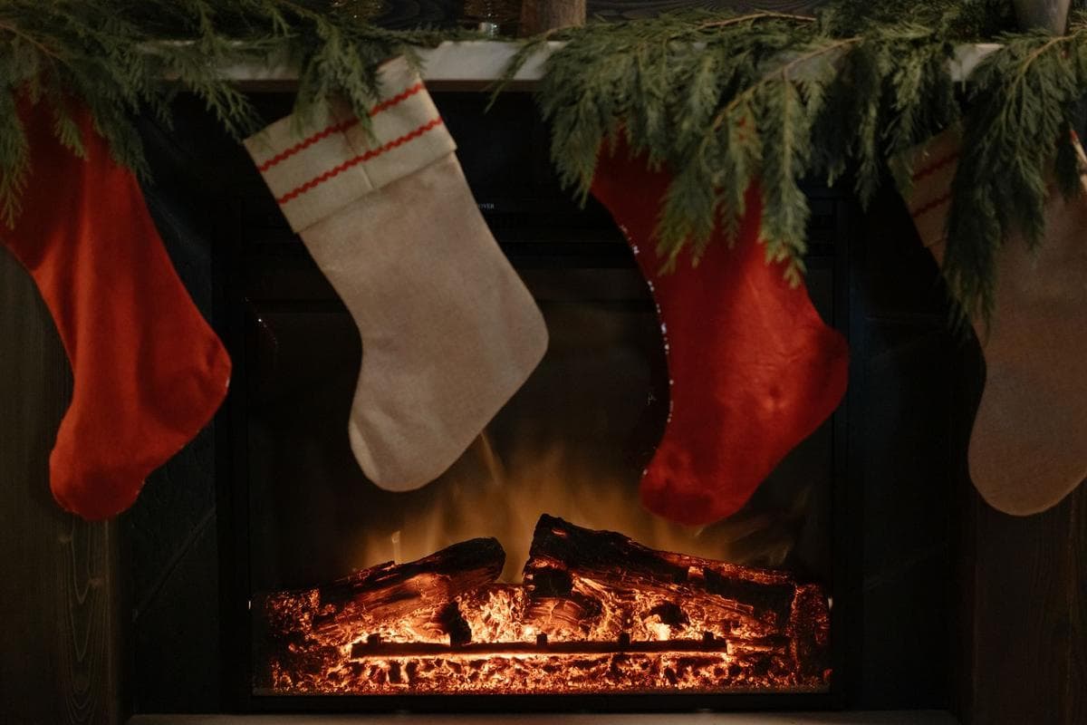 Christmas stockings hanging from a mantel with evergreen garland above a glowing fireplace