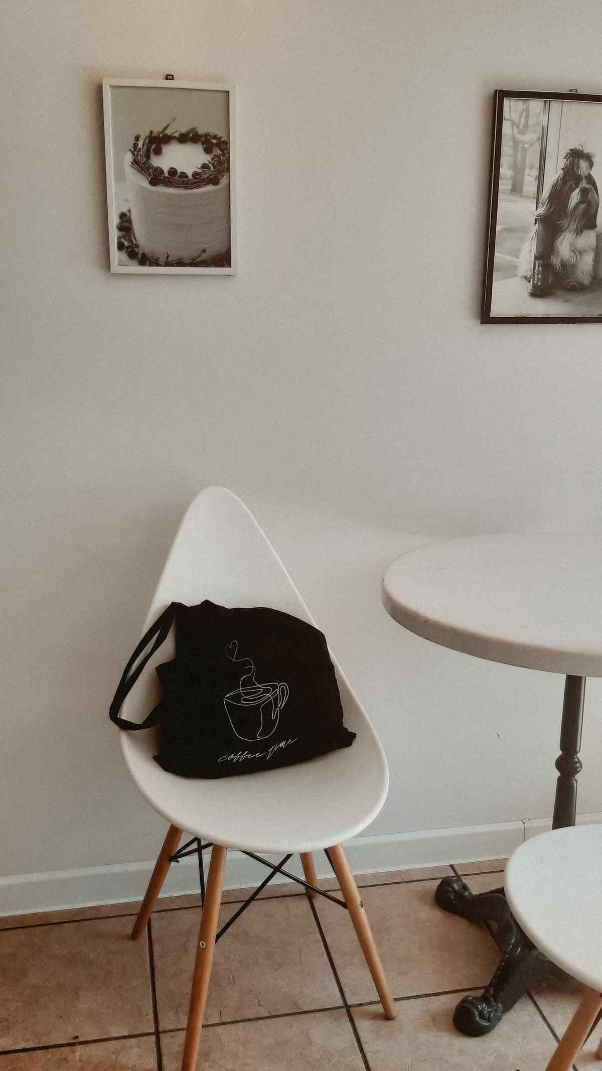 Two framed black-and-white photographs, one of a cake, hanging above a small round table and white chair in an eating area