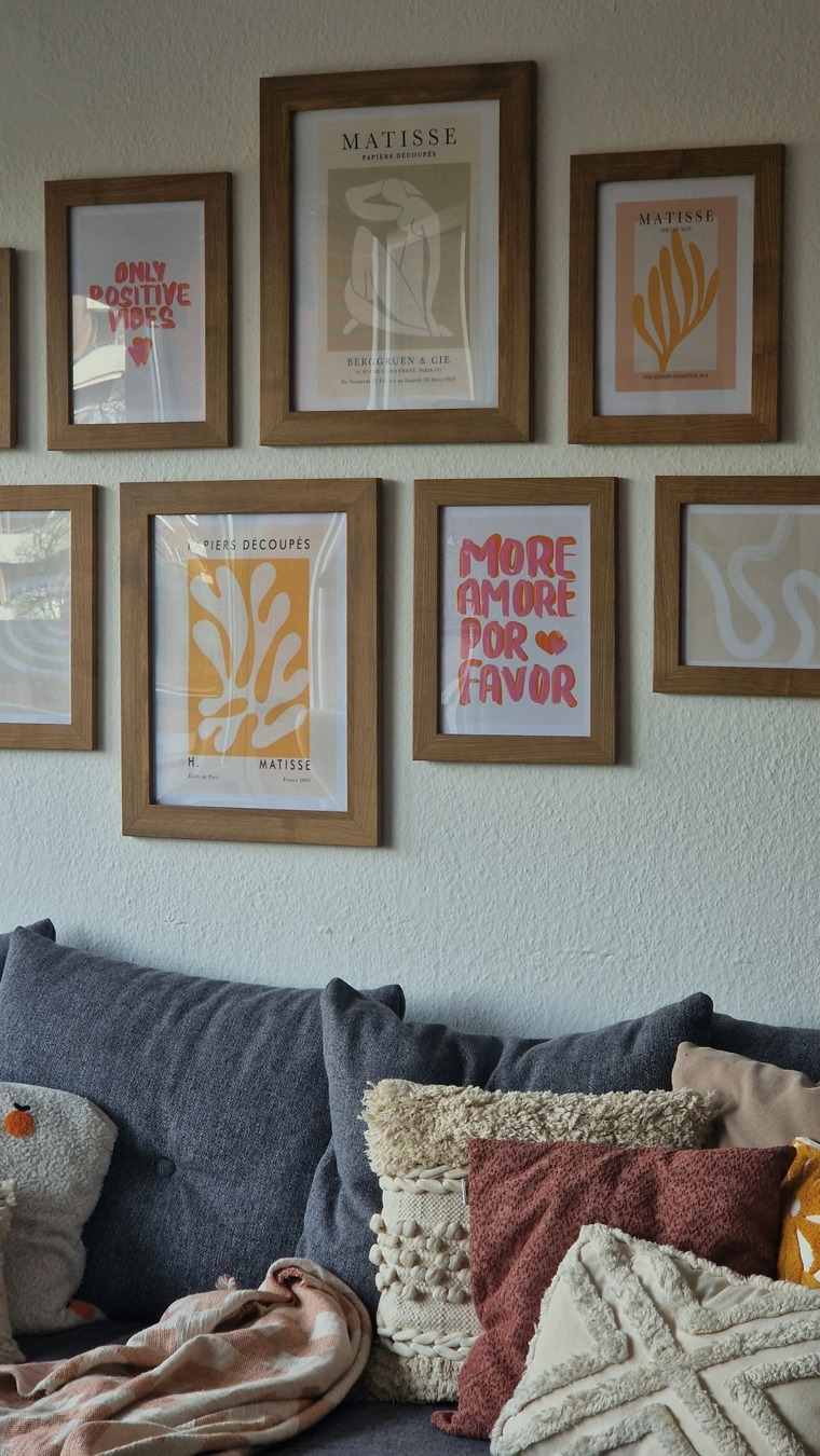 Gallery wall of framed prints in wood frames arranged above a sofa with cushions