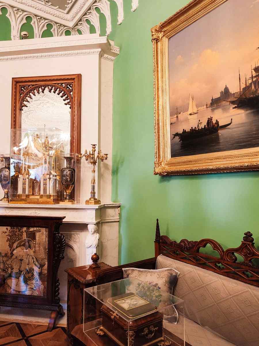 Large seascape painting in an ornate gilt frame on a green wall in a traditional room with a marble fireplace