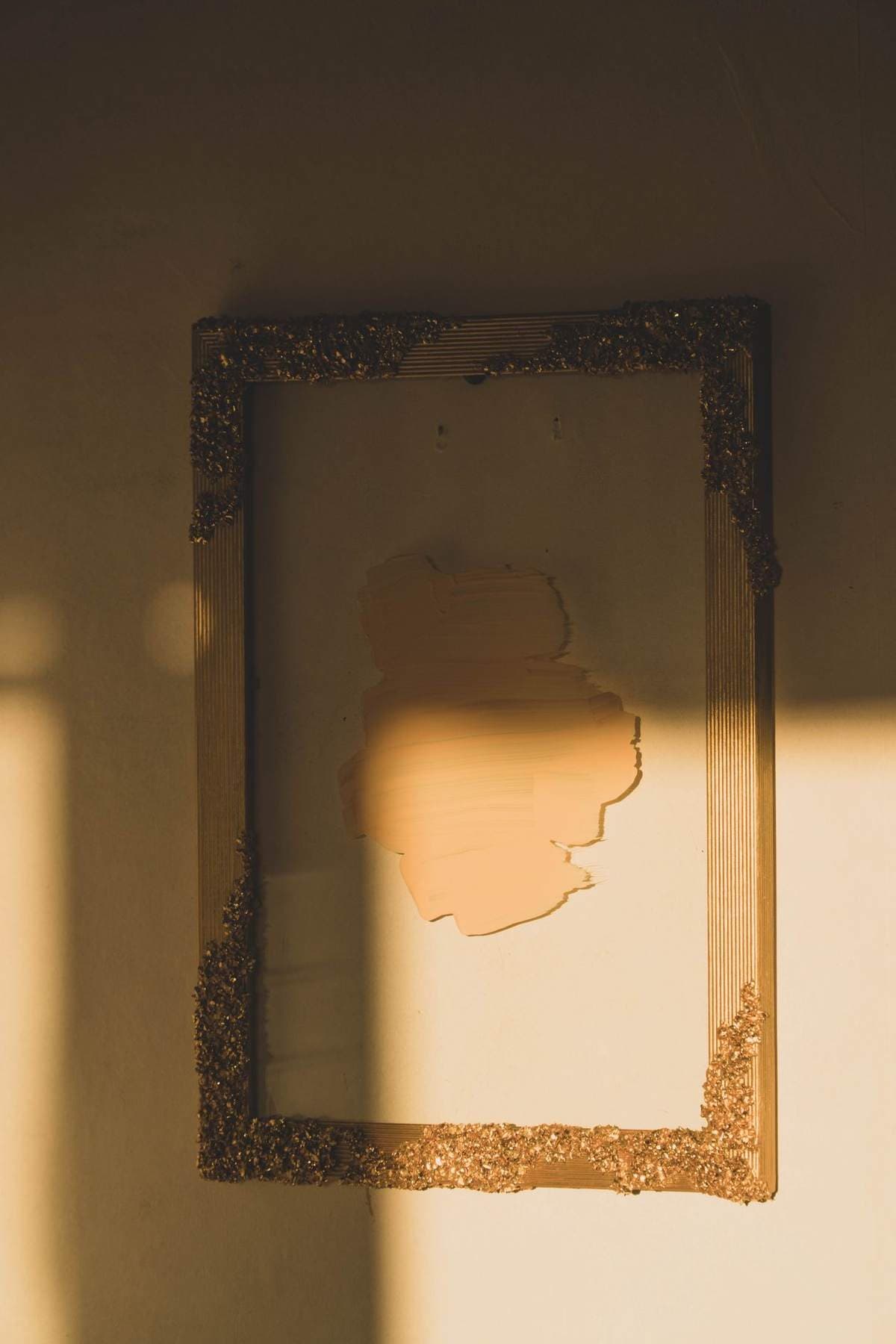 An ornate gold picture frame hanging on a wall in warm sunlight