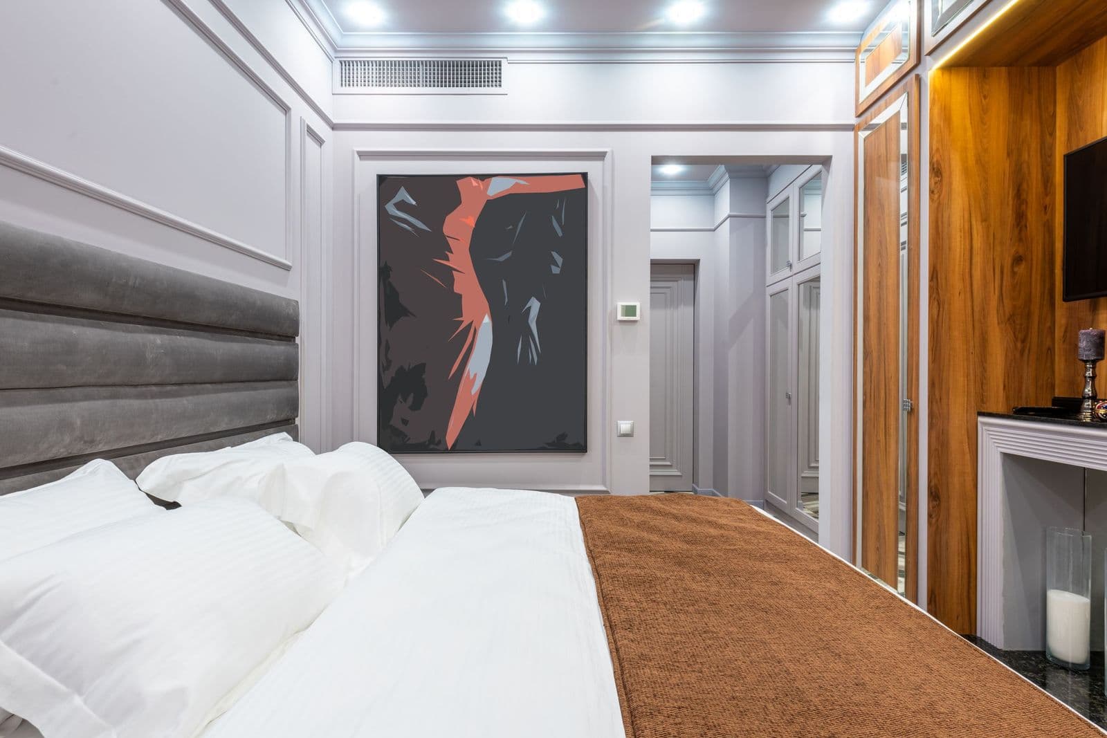 A hotel guest room with a large painting hanging on the wall at the foot of the bed.