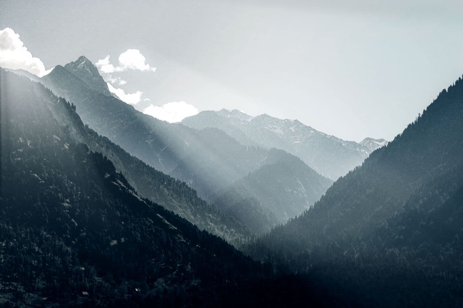 Sunbeams breaking over layered, forest-covered mountain ridges fading into blue mist.