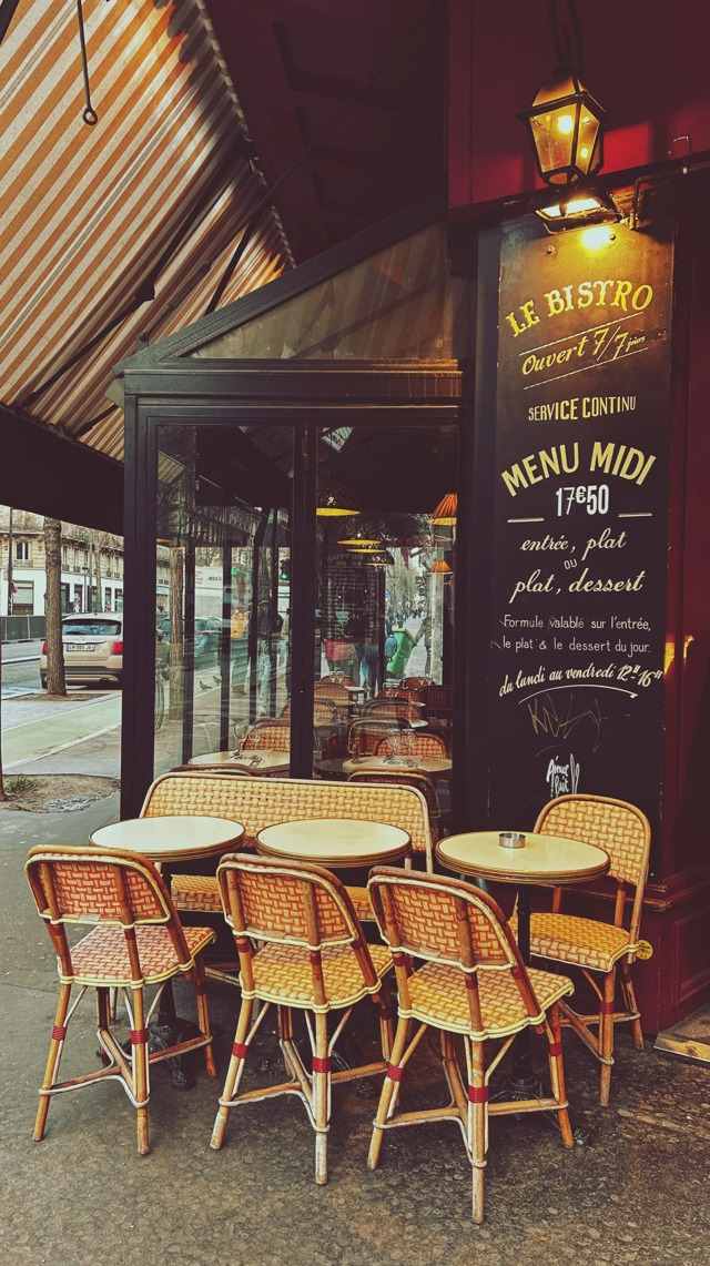 Paris bistro terrace with rattan chairs and small round tables beside a chalkboard menu