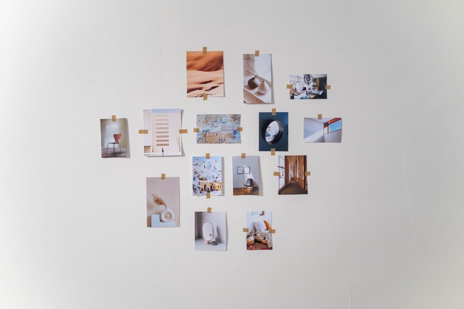 Unframed photos and prints taped to a white wall in a loose grid, a no-nails display that leaves rented walls undamaged.