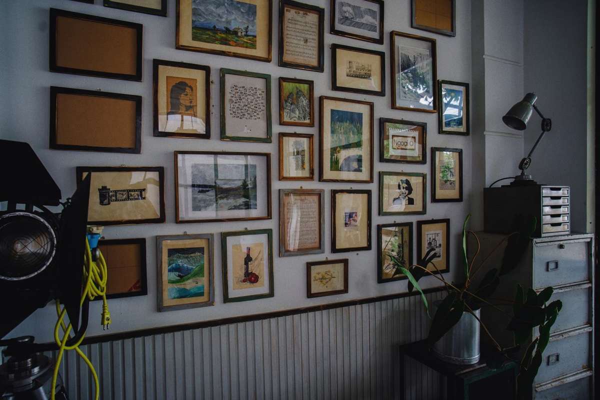 A dense salon-style gallery wall of many framed pictures and artworks above wainscoting in a studio room