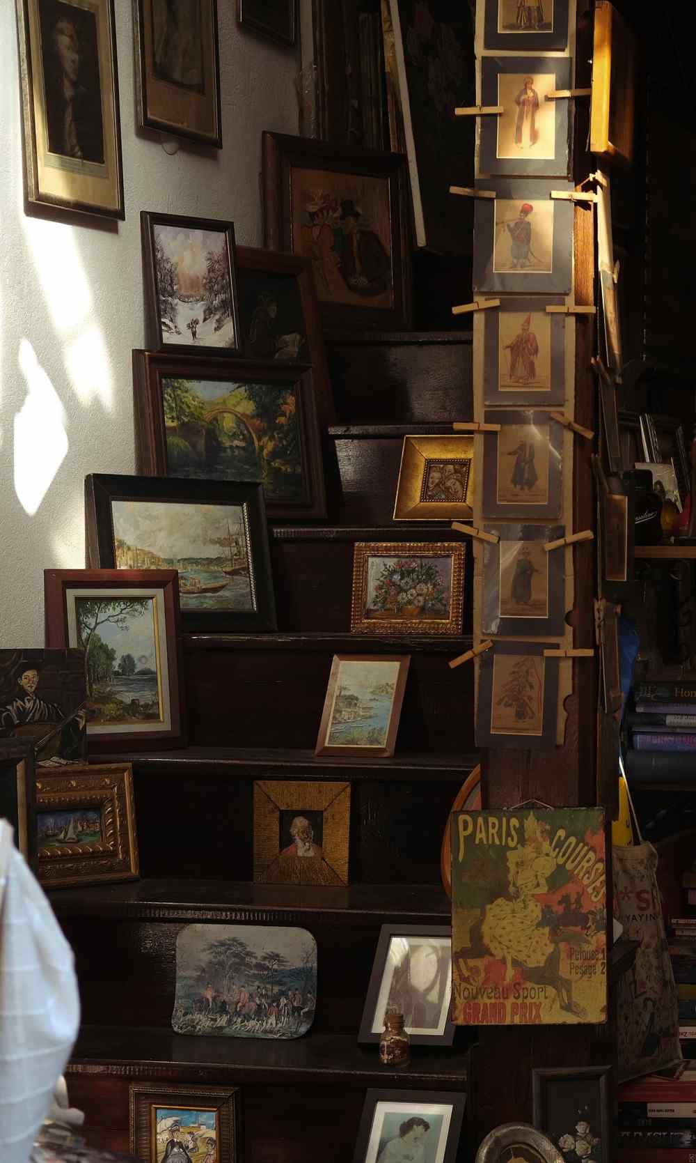 Framed paintings and prints arranged in a stepped climb along a dark wooden staircase