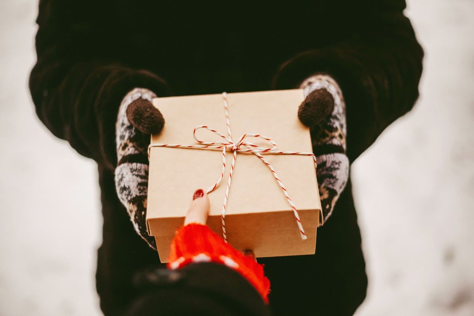 A flat gift wrapped in kraft paper and twine being handed from one person to another.