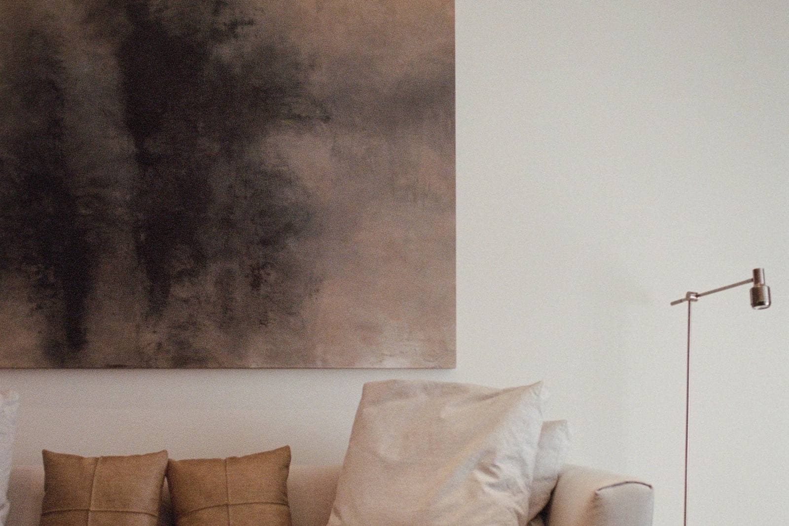 An oversized abstract canvas spanning most of a sofa's width in a neutral living room, its scale set in clear proportion to the furniture below it.