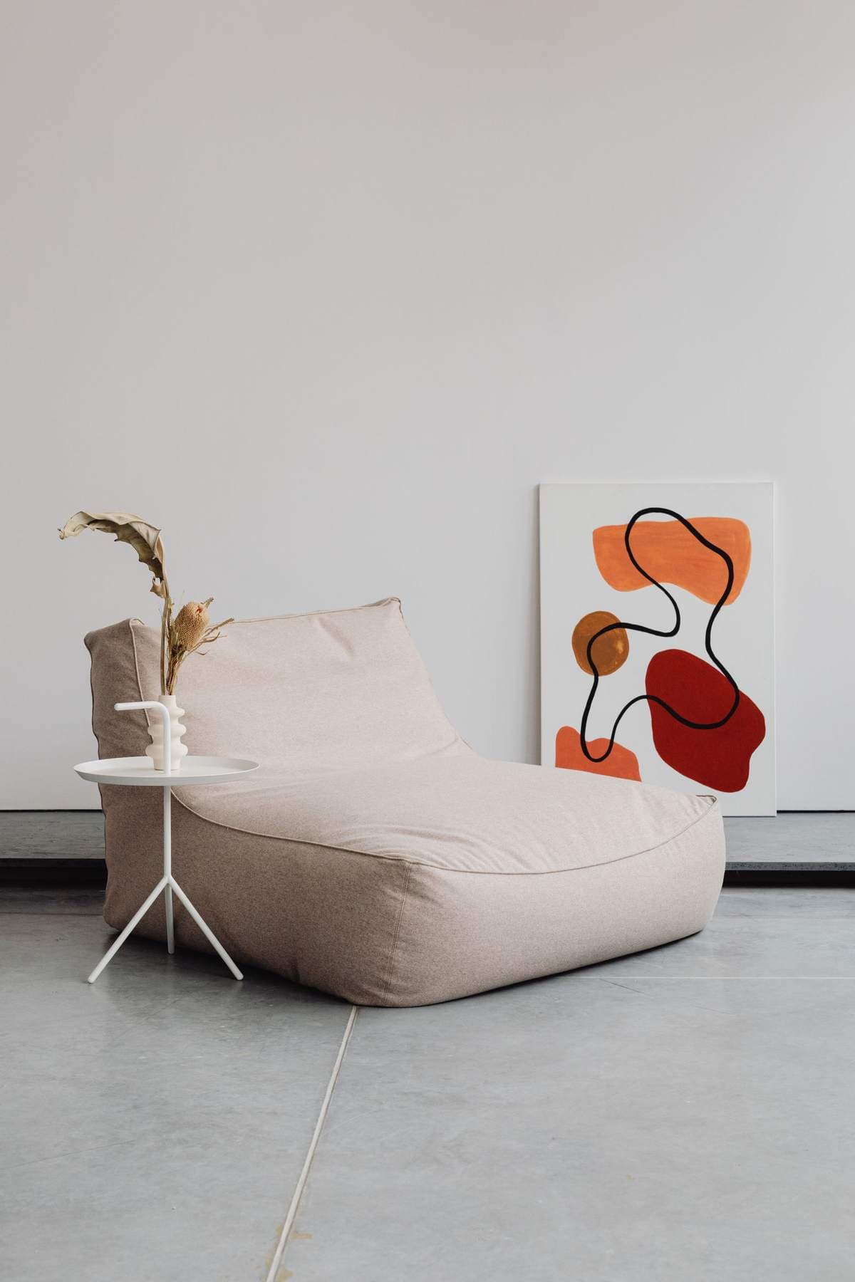 Abstract canvas with orange and red organic shapes leaning against a wall beside a beige lounge chair