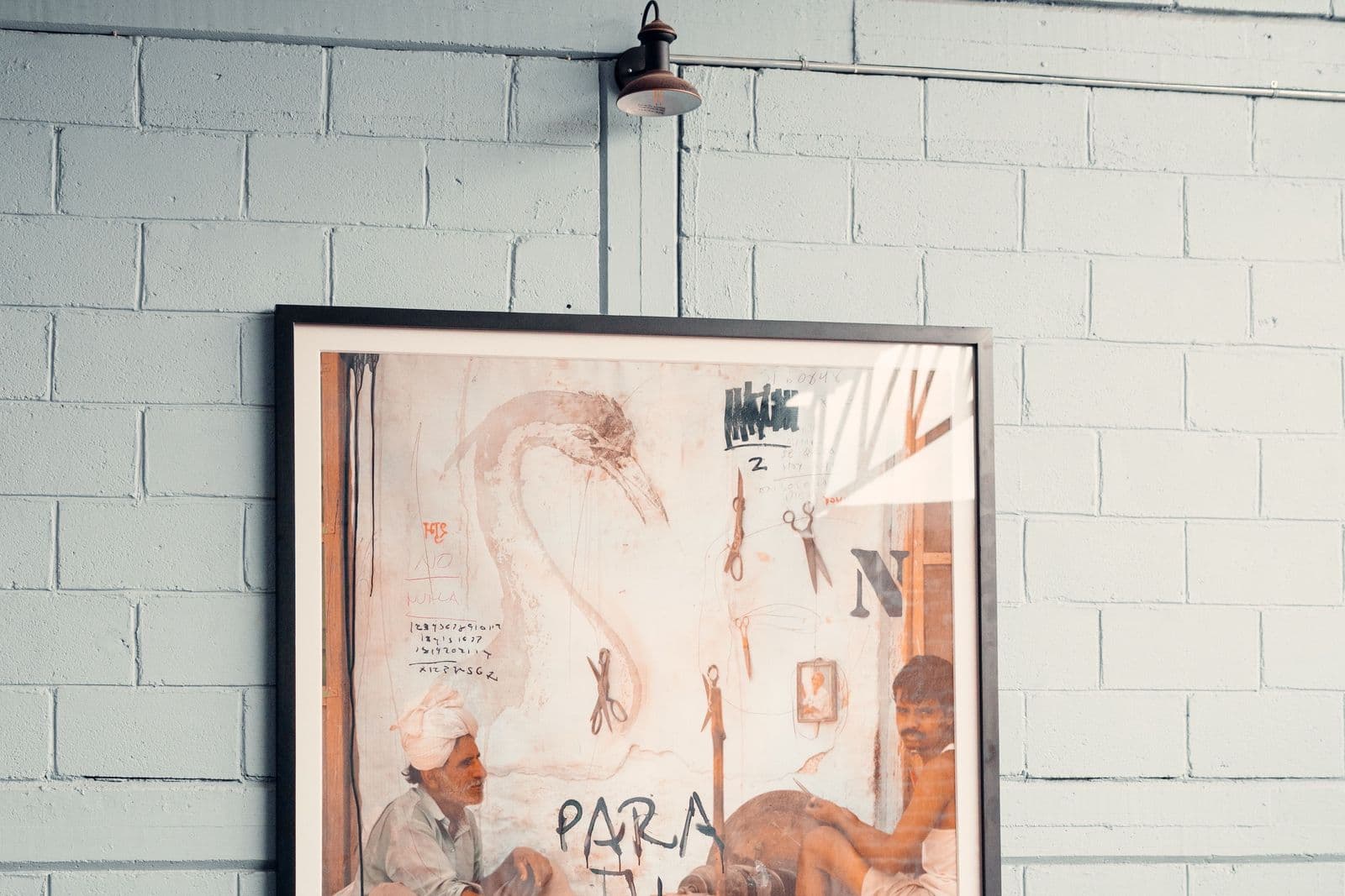 A large painting in a slim dark frame hanging on a pale blue painted brick wall above leather seating in a lounge.