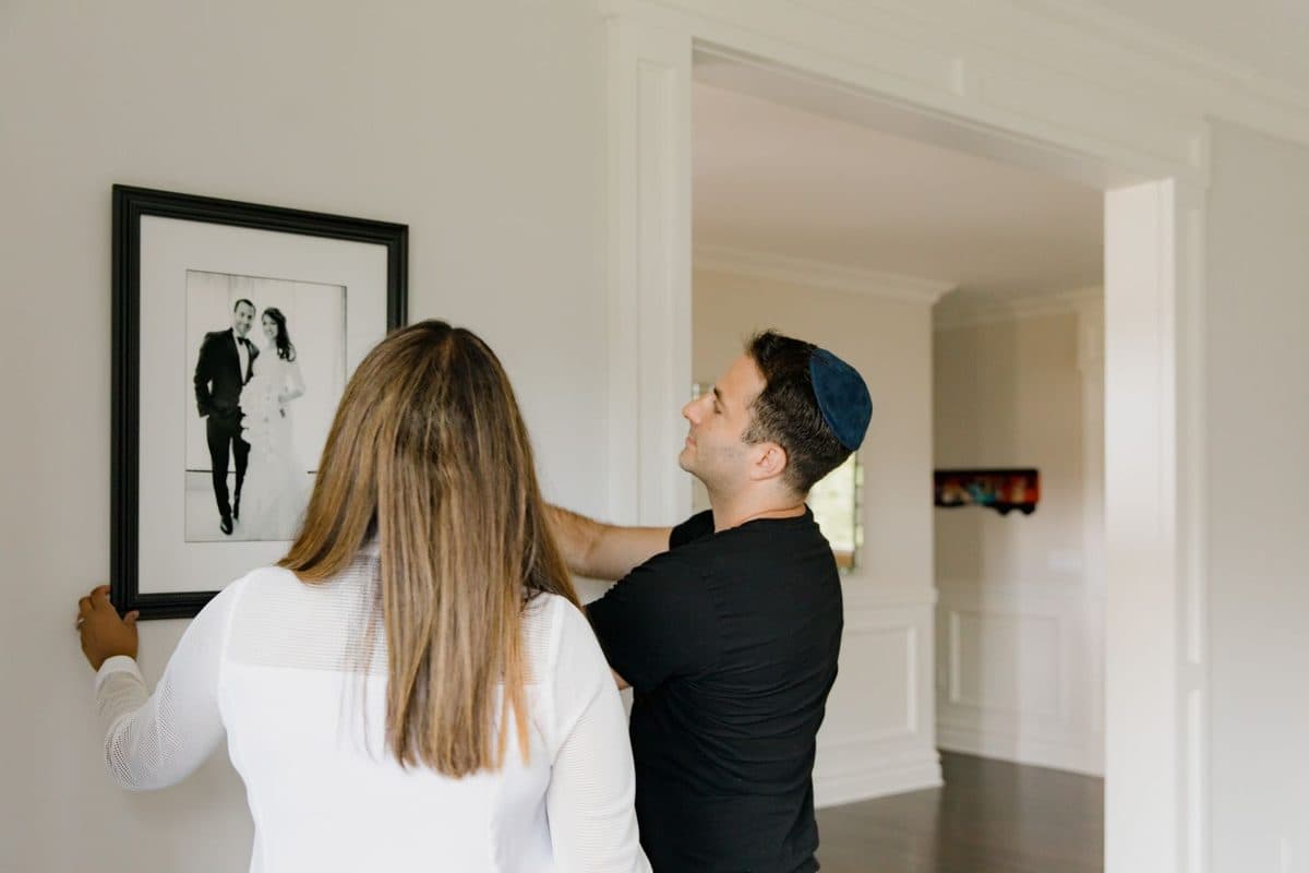 Couple hanging a large framed black-and-white wedding portrait on a white wall at home