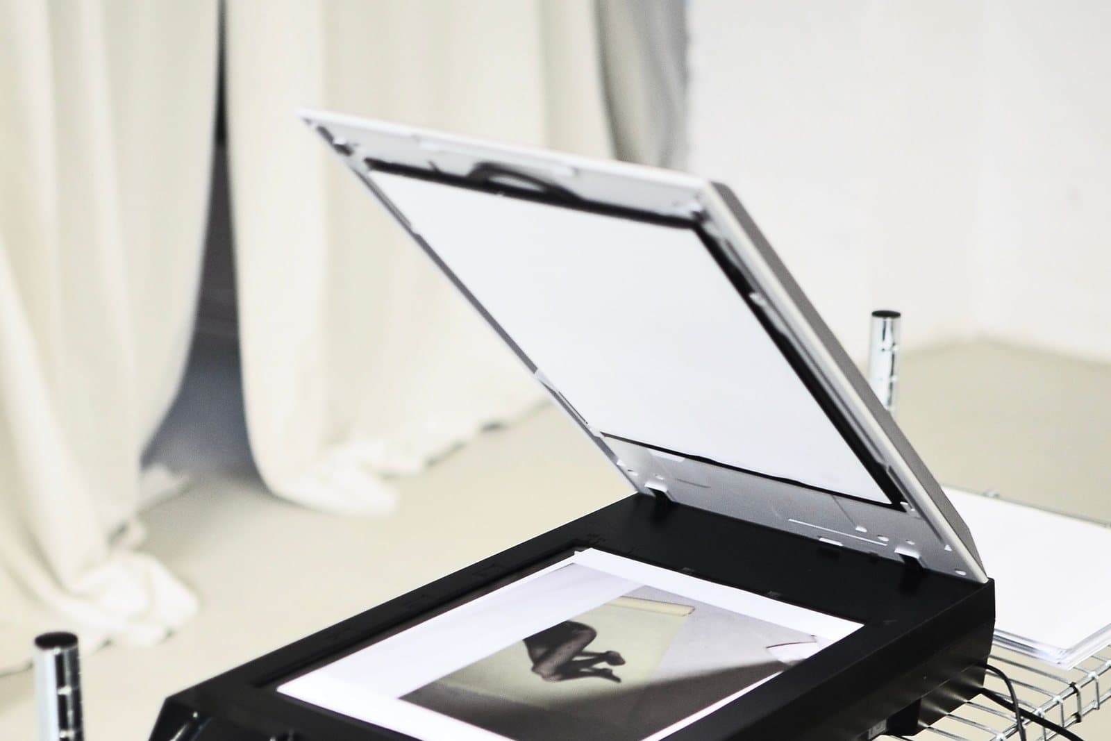 An open flatbed scanner with a black-and-white photograph on the glass, ready to digitize.