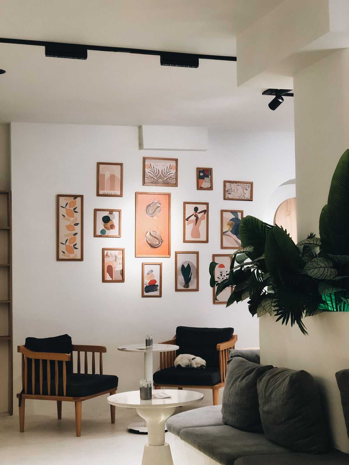 Gallery wall of framed prints in different sizes viewed across a bright lounge with armchairs and a sofa