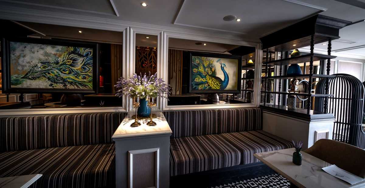 A hotel lounge with striped banquette seating and large framed peacock paintings on the walls
