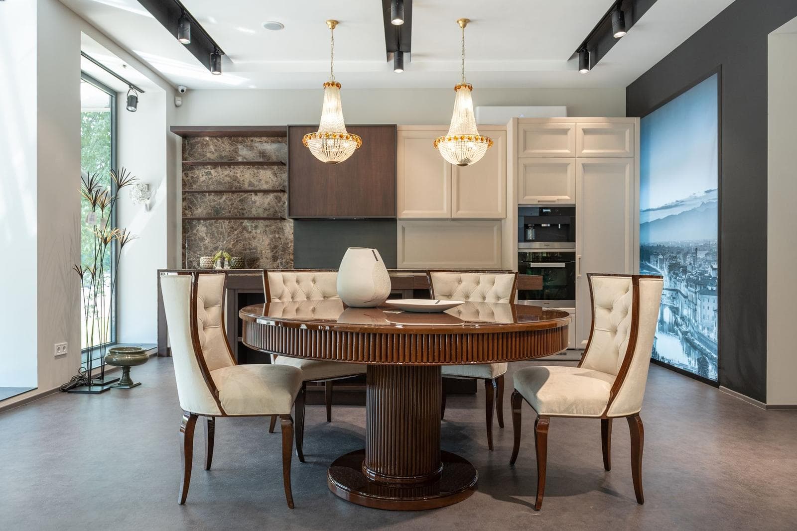 Elegant kitchen-diner with a round dining table under a crystal chandelier and a large landscape panel on the wall.