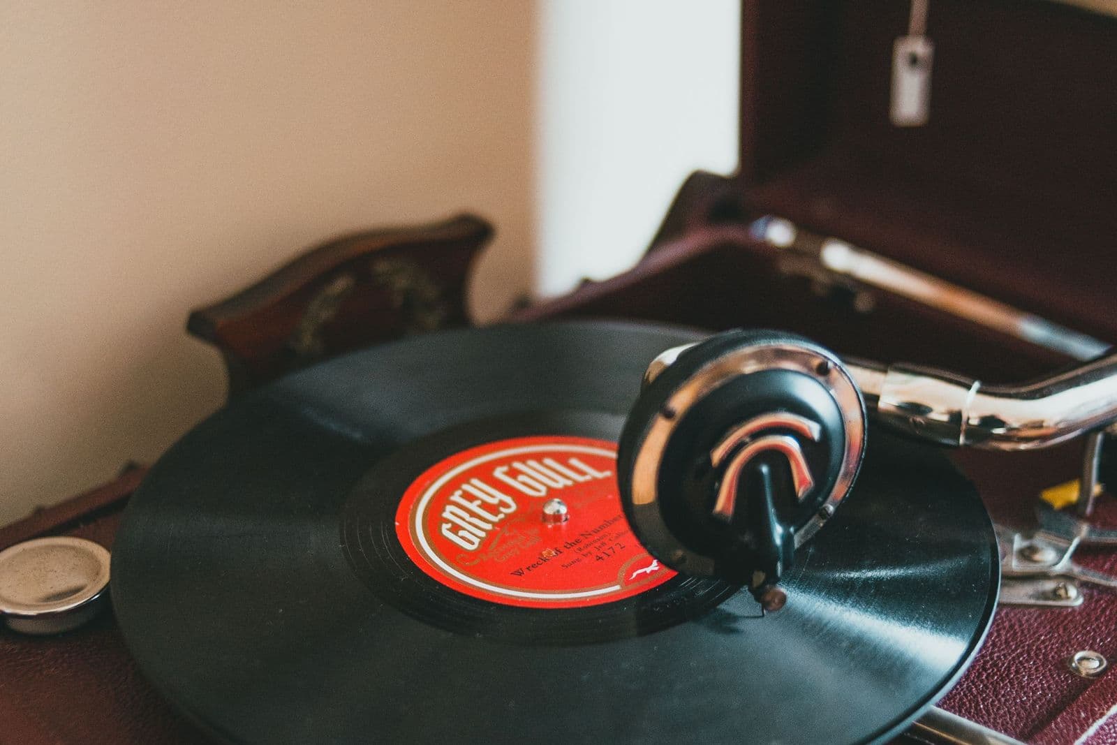 A vintage wind-up gramophone with a vinyl record on its turntable beside a bright window.
