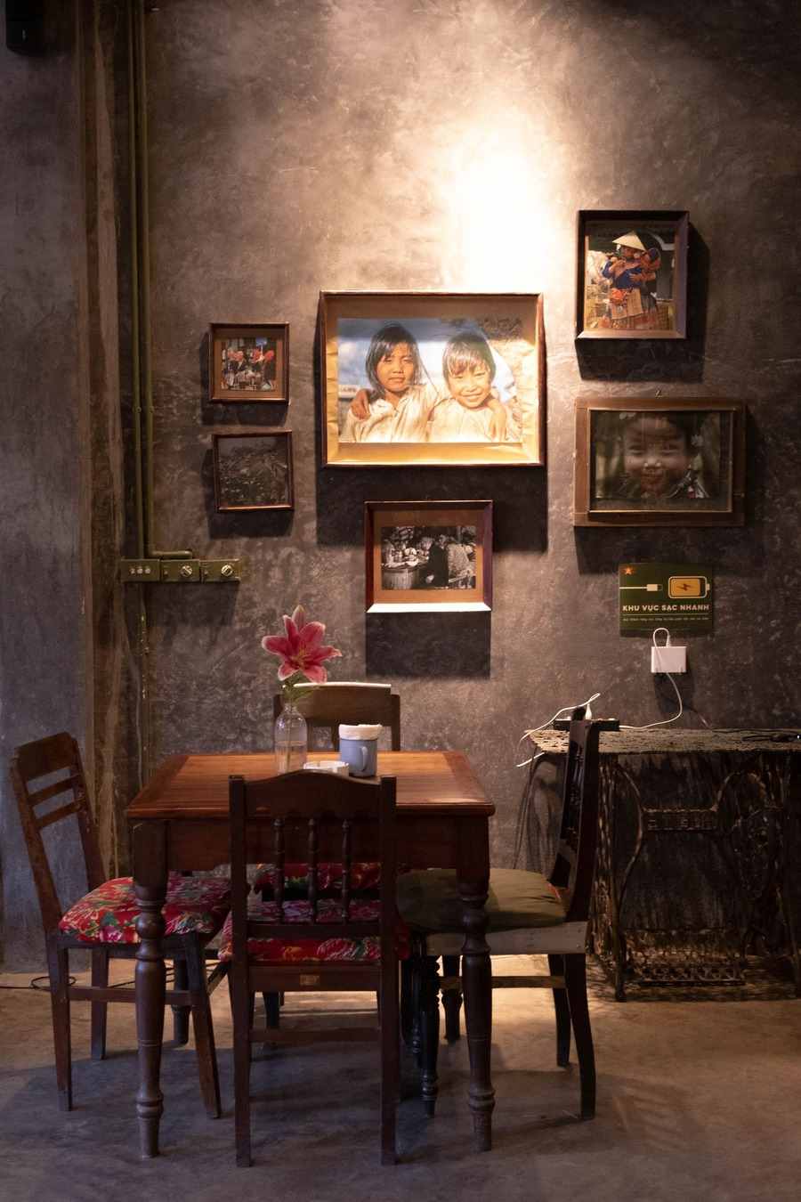 A set of framed portrait photographs of different sizes arranged together on a dark concrete wall above a wooden table