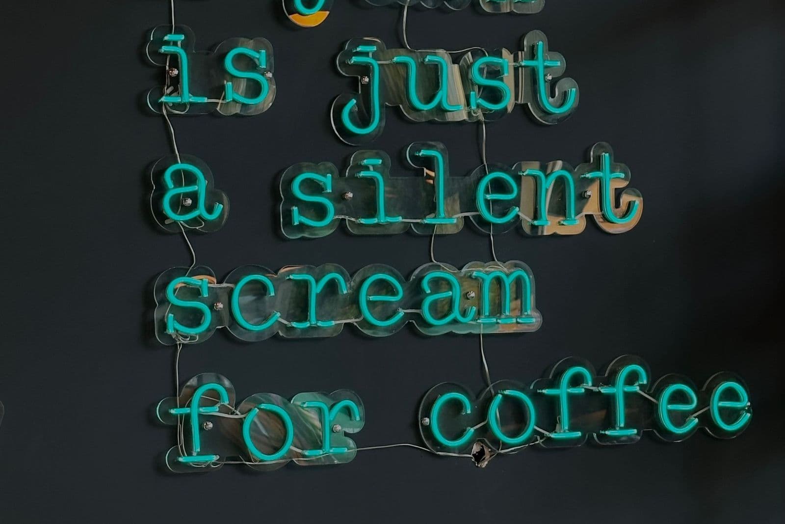 Teal neon lettering spelling out a coffee quote mounted as wall decor on a dark wall.