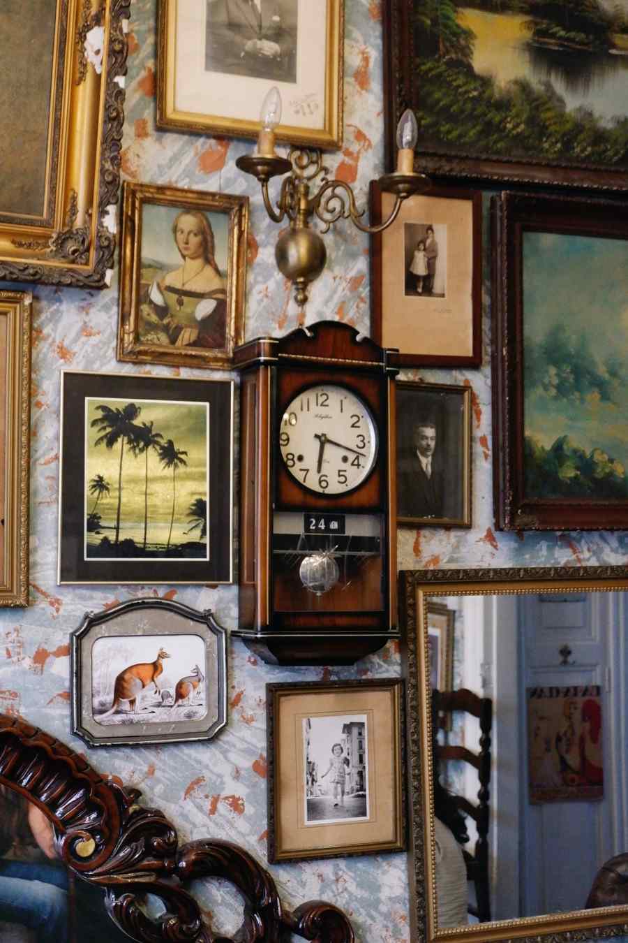 Wall covered with vintage framed portraits, paintings and photographs around an antique wooden wall clock